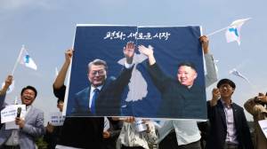 supporters carry banner featuring Moon Jae-In and Kim Jong-Un with unification theme